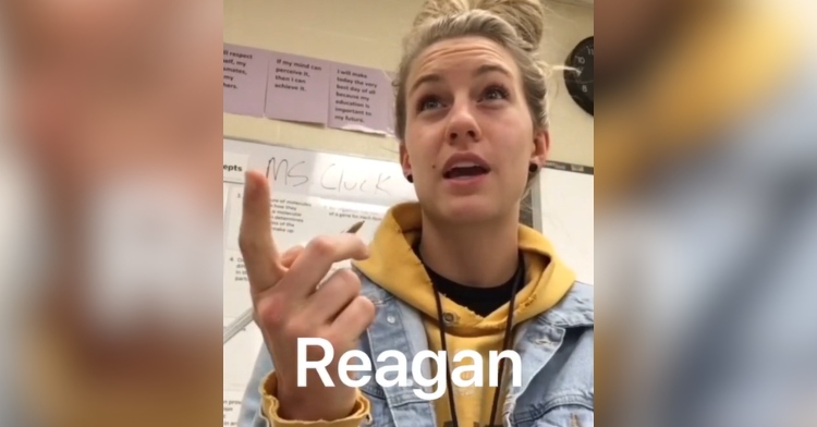 A young woman sits at a desk in a classroom. She's pointing at someone off camera as she talks. Text on the image reads: Reagan.