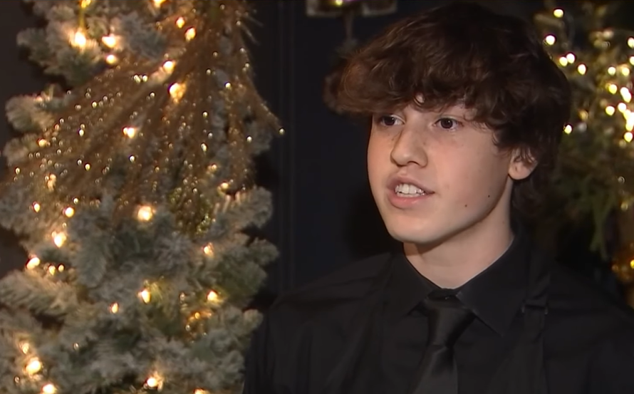 Teen busboy, Jackson Teran, talks to news crew near a tree lit with Christmas lights, recounting how he saved the life of a choking man.