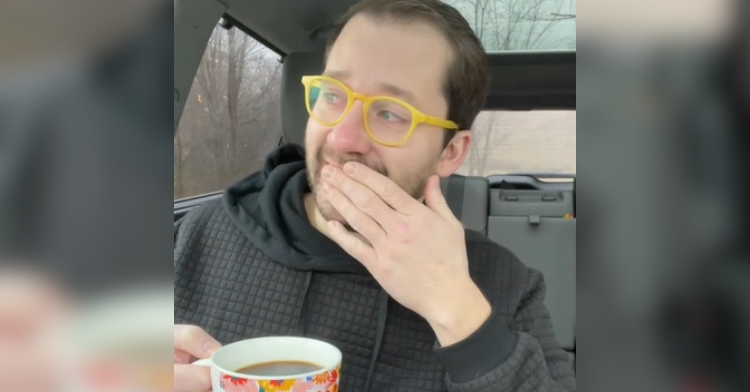 Dillon White looks like he's on the verge of tears as he sits in his car, looking away from the camera. He holds a hand to his mouth as the other holds a cup of coffee.