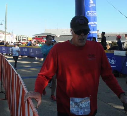 A man named Michael looks exhausted, mouth open, after crossing the finish like of a half-marathon.