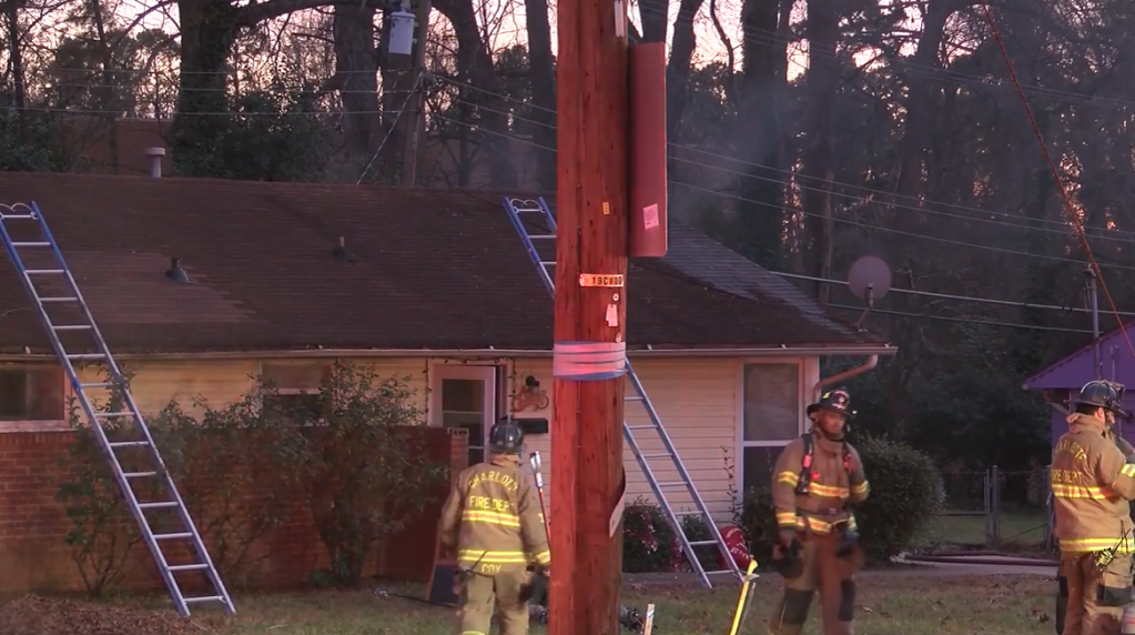 Three firefighters walk around outside of a home that was just on fire.