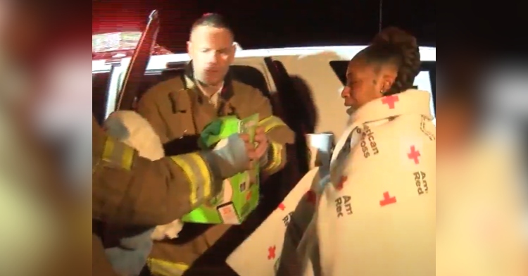 North Carolina mom stands next to a firefighter vehicle wrapped in an American Red Cross blanket. One firefighter is handing a toy to another firefighter.