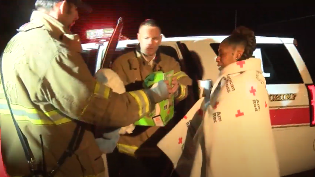 North Carolina mom stands next to a firefighter vehicle wrapped in an American Red Cross blanket. One firefighter is handing a toy to another firefighter.