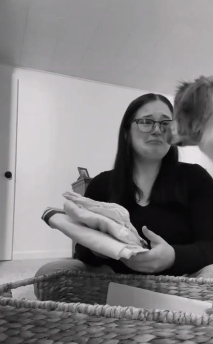 Dog looks to comfort Mom who recently had a miscarriage. Mom sits on the floor, holding a baby blanket, crying.