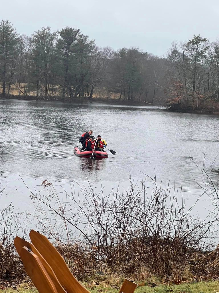 Three people on a small boat row their way on a lake to a small island in Rhode Island for a dog rescue.