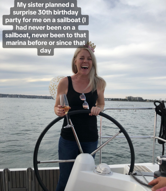 Brooke smiles, as closed, as she stands on a sailboat, wheel in one hand and a drink in the other.
Text on the image reads:
My sister planned a surprise 30th birthday party for me on a sailboat (I had never been on a sailboat, never been to that marina before or since that day