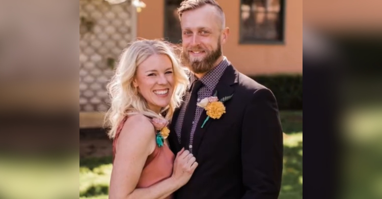 A woman and man smile as they pose together outside. She's wearing a nice dress and he's in a suit.