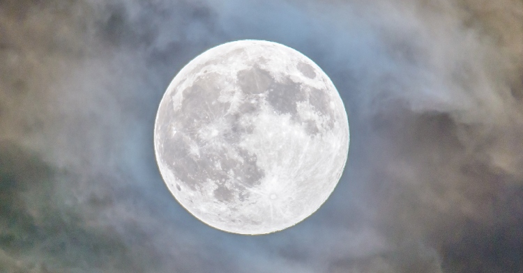 Detailed view of a full Moon with lots of clouds surrounding it.