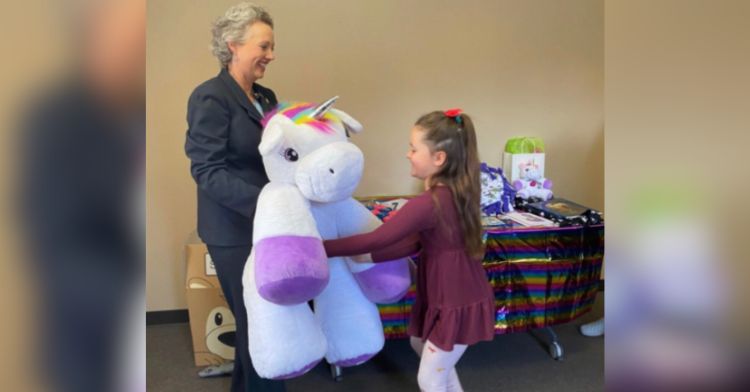 A little girl receives a large unicorn plushie.