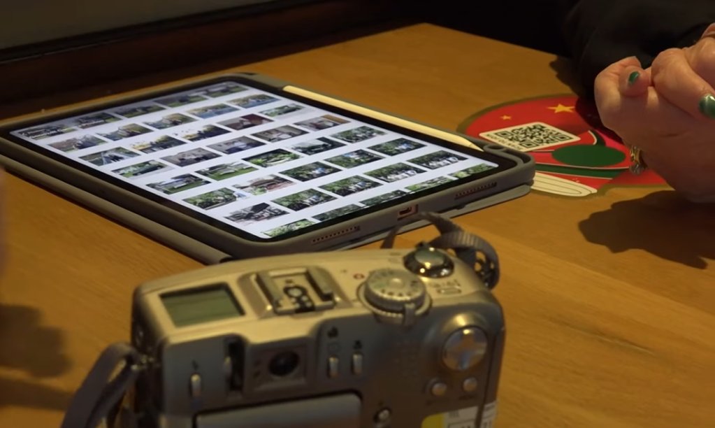 A Goodwill camera sat on a table next to a tablet. On the tablet are a photos.