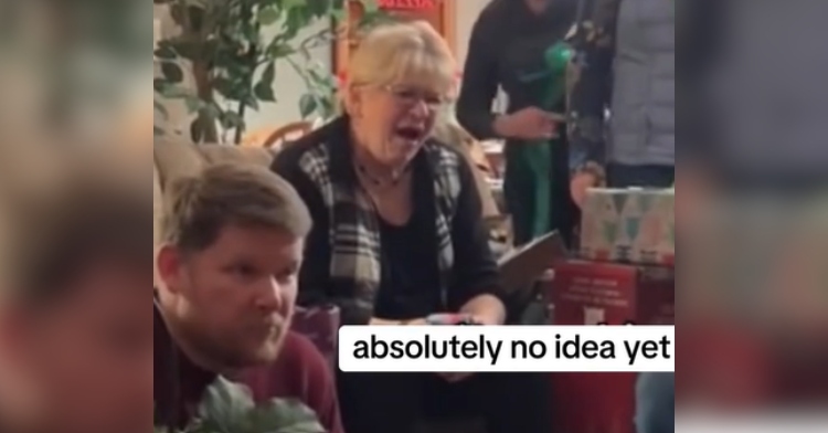 Grandma looks confused over the Christmas prank her grandkids pulled. She sits on a chair, mouth open. Text on the screen reads "absolutely no idea yet"