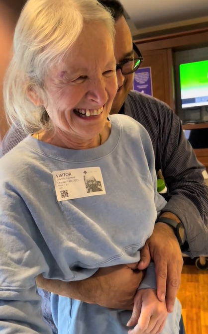 Grandma smiles as someone helps her walk closer to her newborn grandson who can't be seen in this photo.
