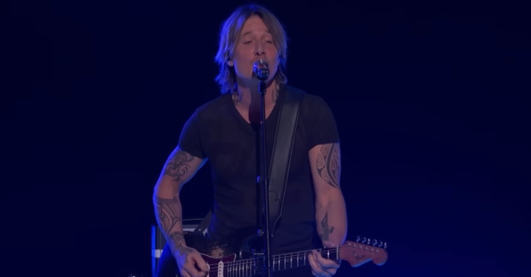 Keith Urban sings "Blue Ain't Your Color" on "The Voice." He's playing electric guitar and the lighting around him is a dark blue.