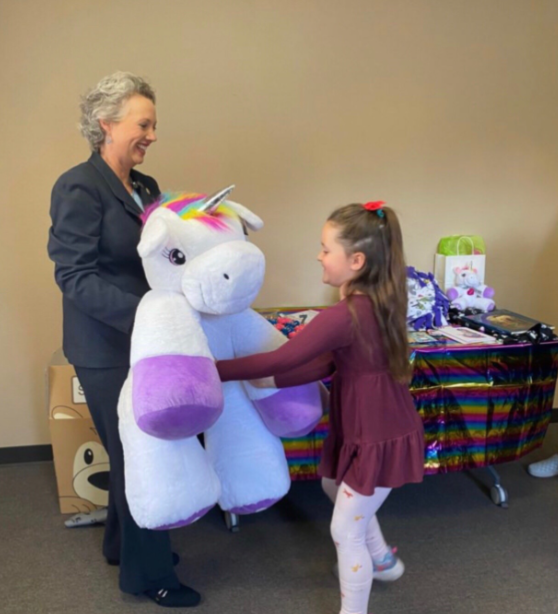 A little girl receives a large unicorn plushie.
