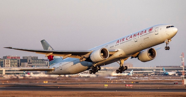 View of an Air Canada plane that is just barely taking off the ground, the nose of the plane aiming toward the sky.