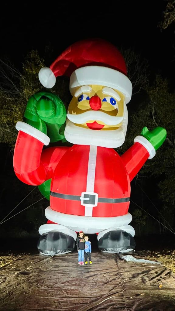 View of the mysterious inflatable Santa that showed up in a Texas neighborhood. For scale, two kids stand and smile at the feet of the inflatable, and their heads appear to line up with the top of the shoes.