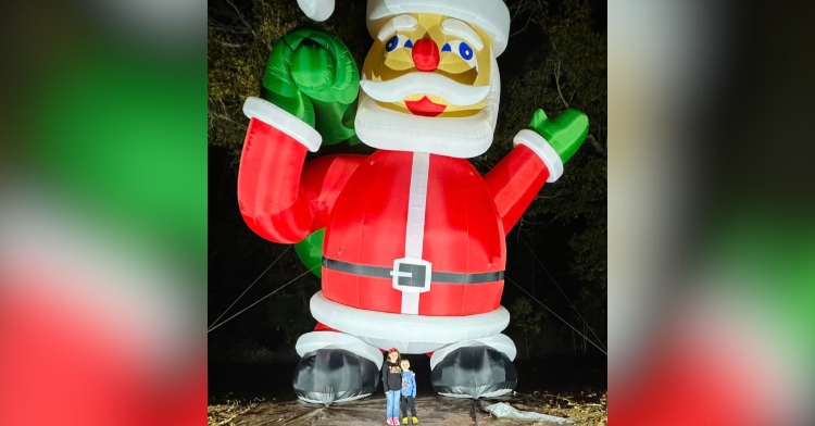 View of the mysterious inflatable Santa that showed up in a Texas neighborhood. For scale, two kids stand and smile at the feet of the inflatable, and their heads appear to line up with the top of the shoes.