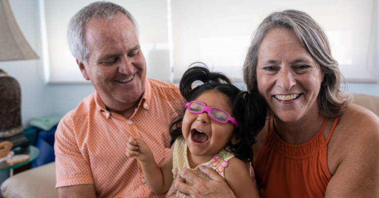 Retired couple holds their adopted disabled toddler and smile at her.