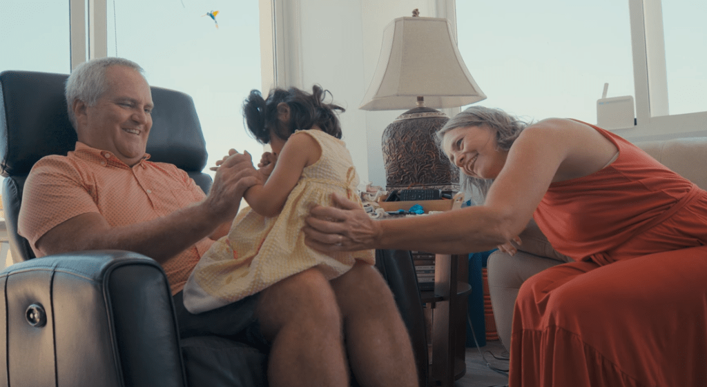 Retired couple Loren and Joan smile as they hold their adopted disabled toddler.