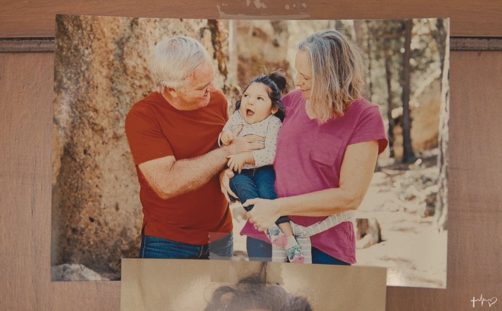 Retired couple holds their adopted disabled toddler and smile at her.