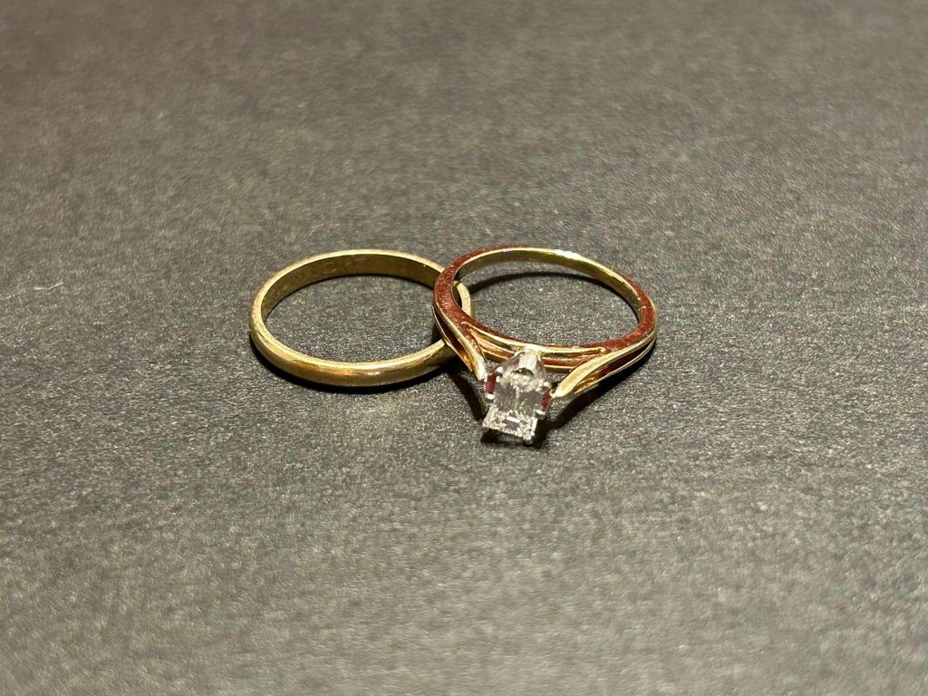 Close up of a wedding band and an engagement ring with a square diamond. The bands are gold.