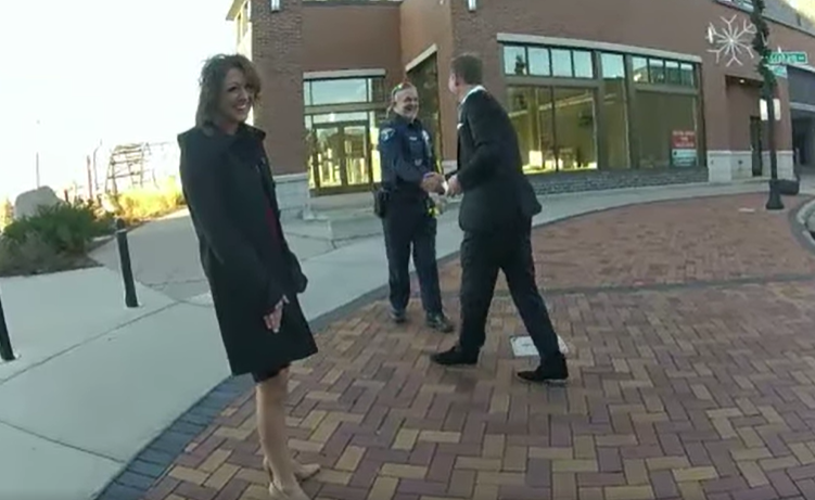 A man shakes the hand of a police officer while his girlfriend smiles. 