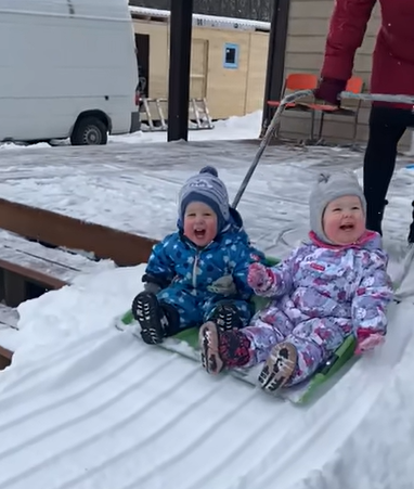 Laughing toddlers getting a ride down a snow slide.
