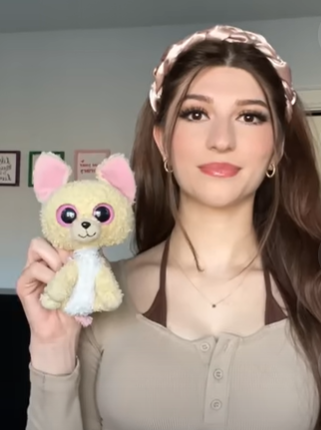 A young woman poses next to her childhood stuffed animal. 