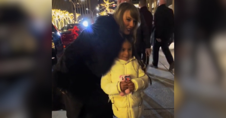 Taylor Swift smiles as she leans down near a little girl to take a photo together.