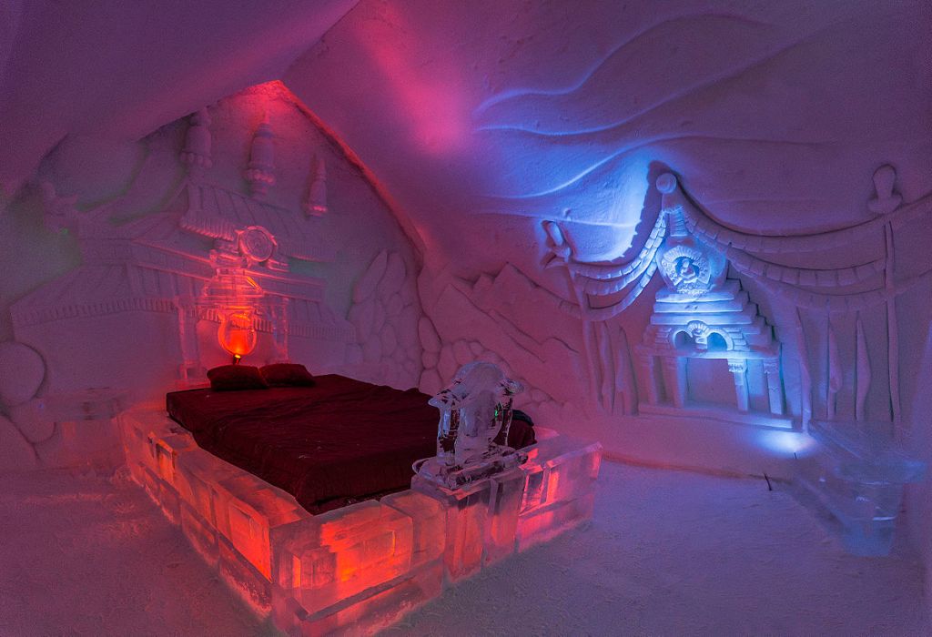 An all ice room in an ice hotel called Hôtel de Glace. The frame of the bed is made of ice and the walls are ice with beautiful carvings.