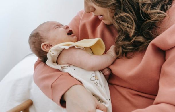 Stock image of a crying infant held in a mother's arms.