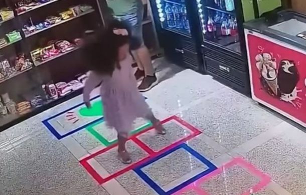 The same store, with a hopscotch board laid out on the tile floor. The young girl is now happily jumping along the squares.