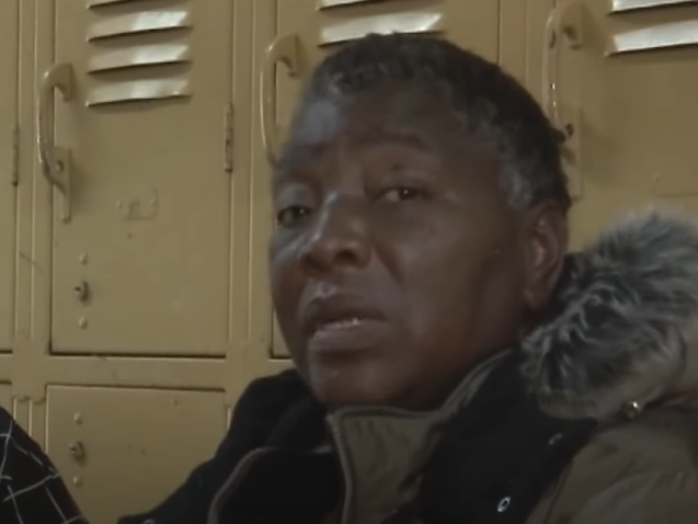Jane Doe wears a winter coat indoors.