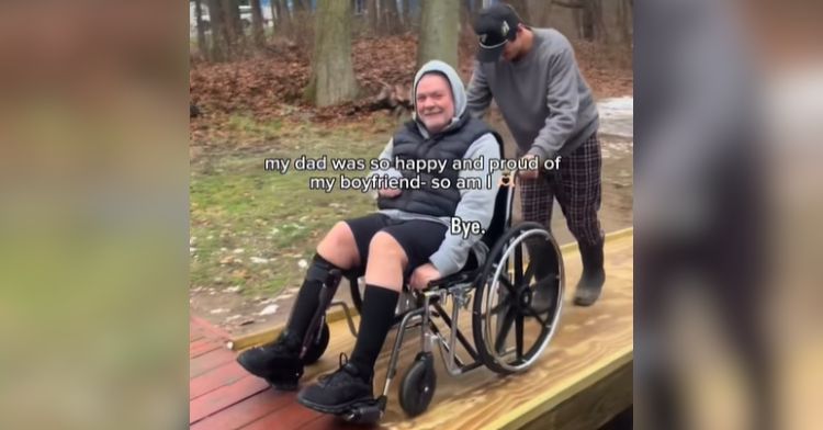 A young man pushes his girlfriend's dad up a wheelchair ramp.