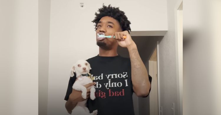 A football player brushes his teeth while holding his little dog.