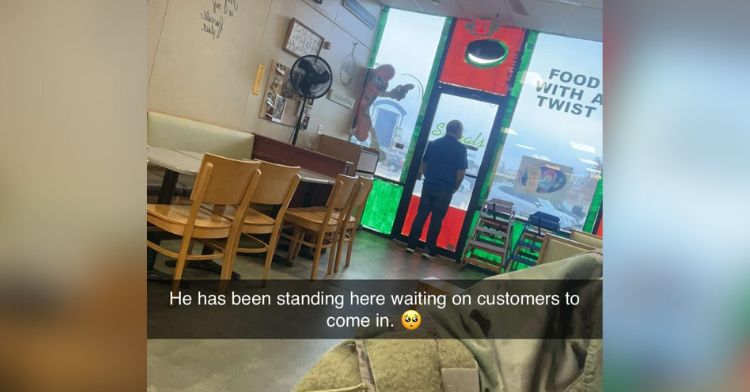 A restaurant owner looking out the front door of his empty hot dog place.