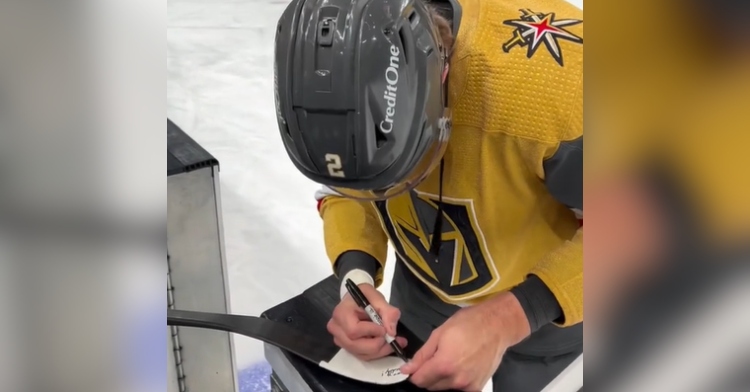 Zach Whitecloud signs a hockey stick after a fan got hit by a puck.