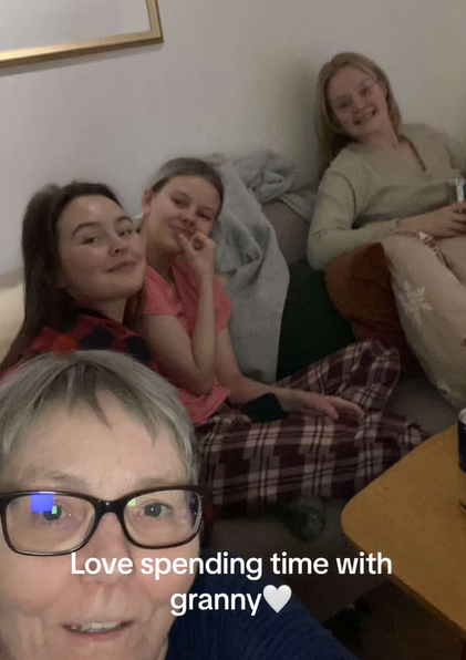 Selfie taken by a grandma. Sitting on the couch behind her are three grandkids, all three of which are smiling.