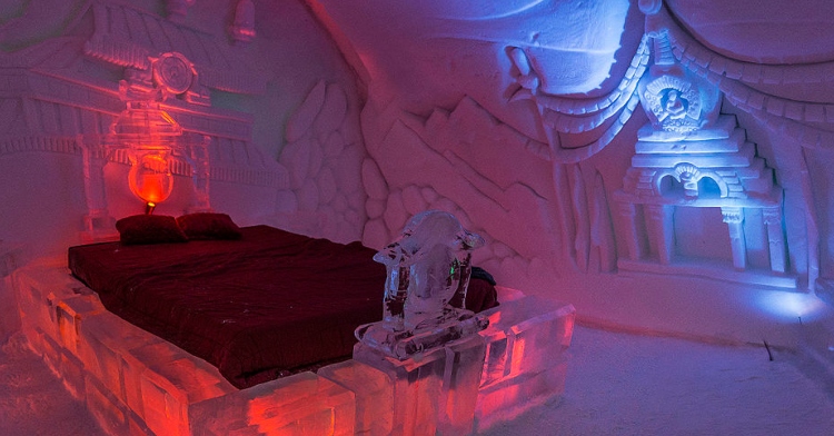 An all ice room in an ice hotel called Hôtel de Glace. The frame of the bed is made of ice and the walls are ice with beautiful carvings.