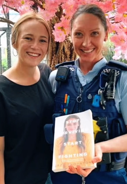 Jazz Thornton smiles and poses with Constable Meika Campbell, the woman who helped save her life. In Meika's hand is a copy of Thornton's book, "Stop Surviving Start Fighting."