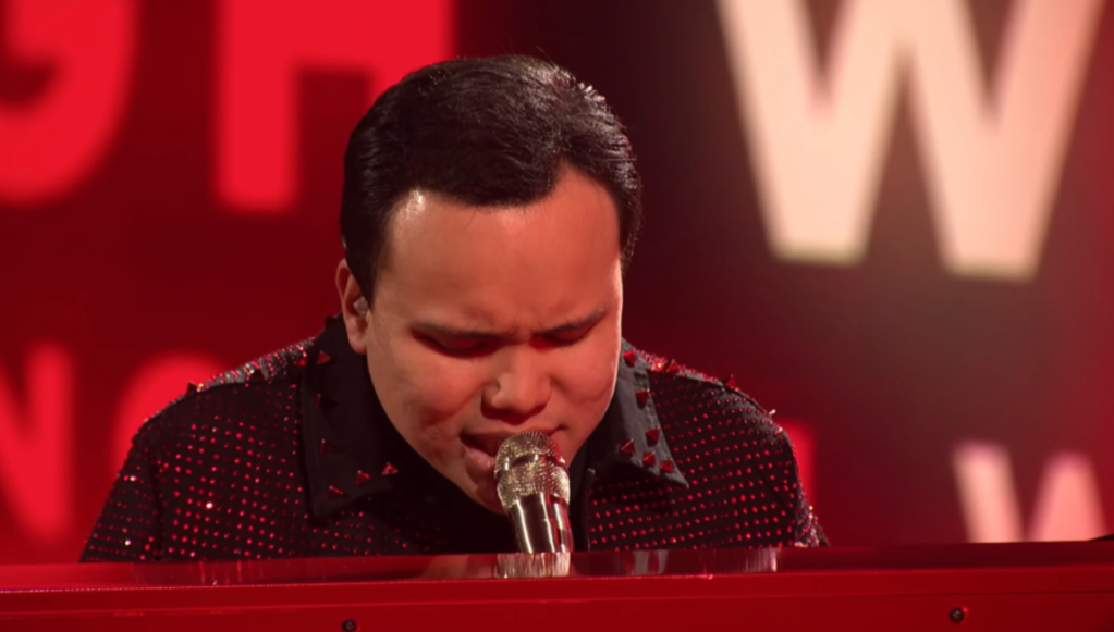 View of Kodi Lee singing into a microphone while playing the piano on "America's Got Talent: Fantasy League."