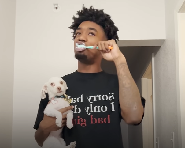 A football player brushes his teeth while holding his little dog.