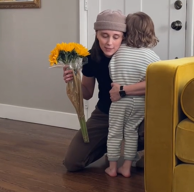 A mom buys yellow flowers for her toddler son. 