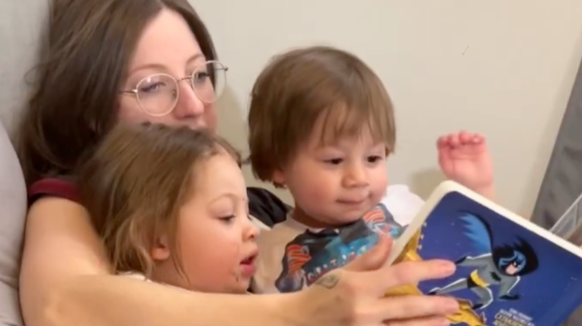 Bridgette Ponson sits with her two kids in her arms as she read them a book.