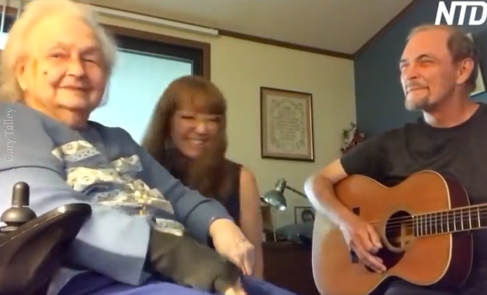 Guitarist from The Box Tops, Gary Talley, smiles at his mom, Nita Talley, as he plays "One Day at a Time" on guitar. A young woman sits between them and smiles as she laughs.