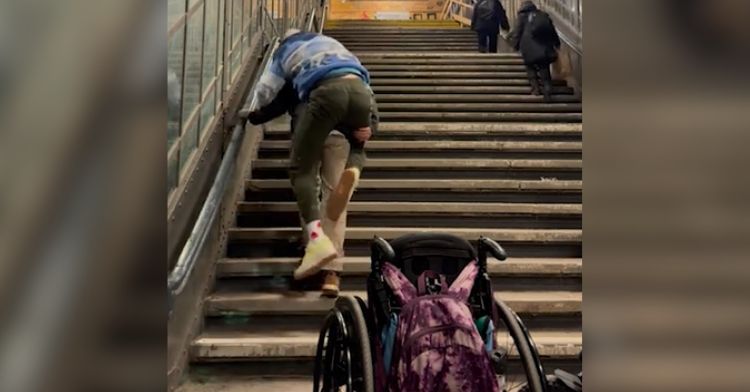 A dad carries his wheelchair-bound son up the stairs.