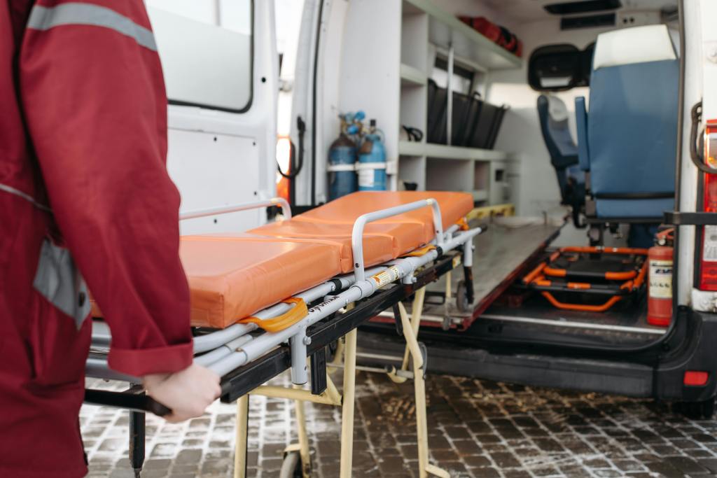 View from behind of someone wheeling an empty gurney into an open ambulance.