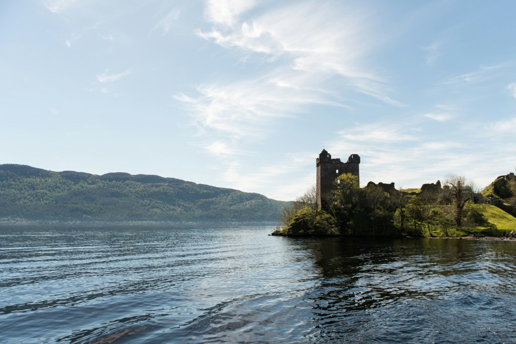 View of a castle in the distance next to the bank of Loch Ness in Scotland.