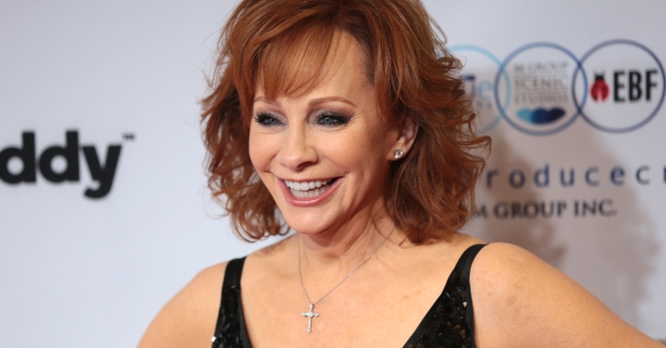 Reba McEntire smiles from ear to ear on a red carpet.