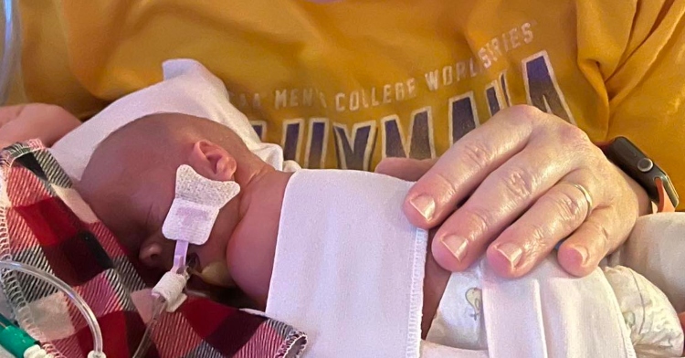 Close up of a preemie baby hooked up to oxygen and sleeping. Mom's hand rests gently on him and is nearly the size of the baby.